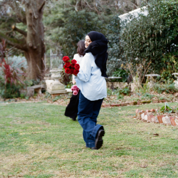 Woman in a hijab carrying a bunch of red roses while walking across a garden lawn.
